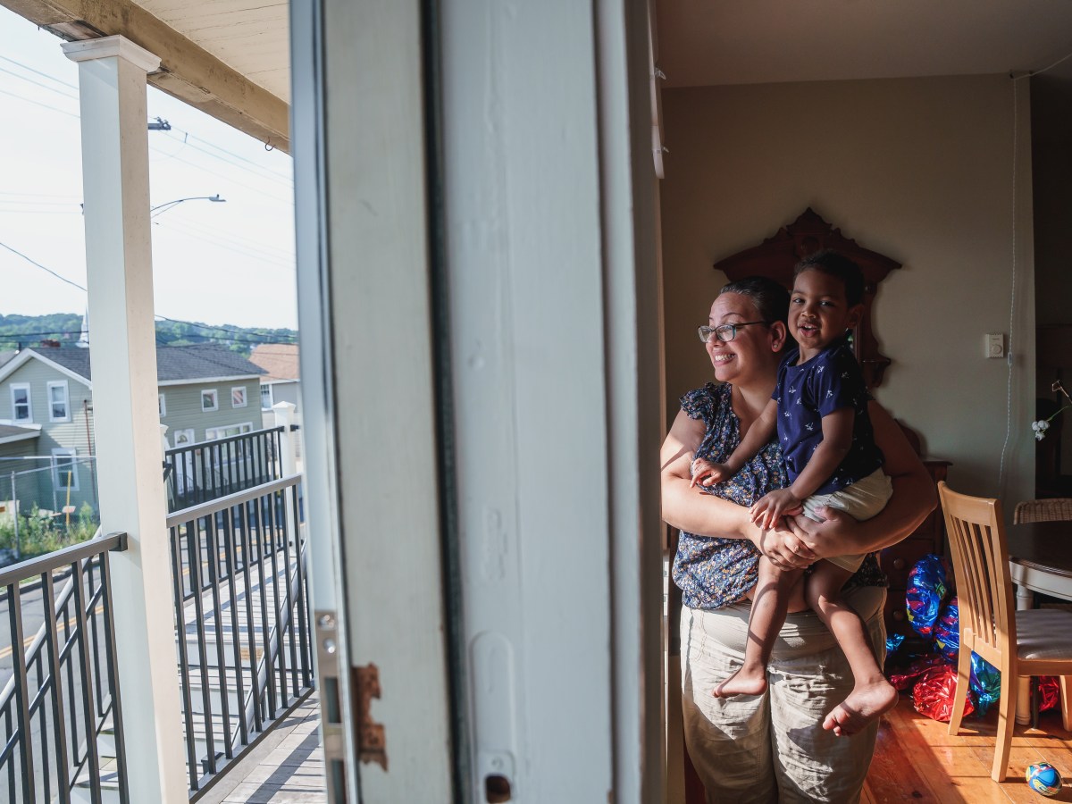 A woman holds a child at the front window of their home.