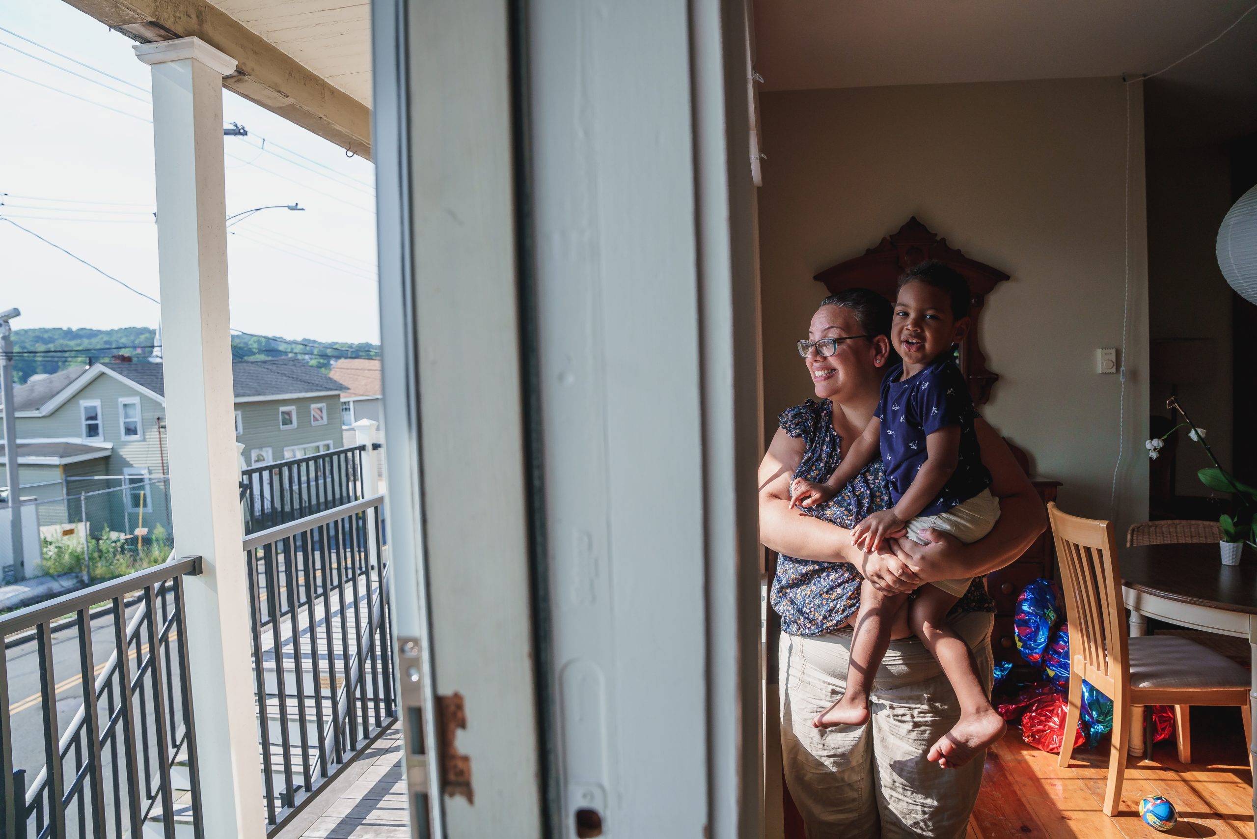 A woman holds a child at the front window of their home.