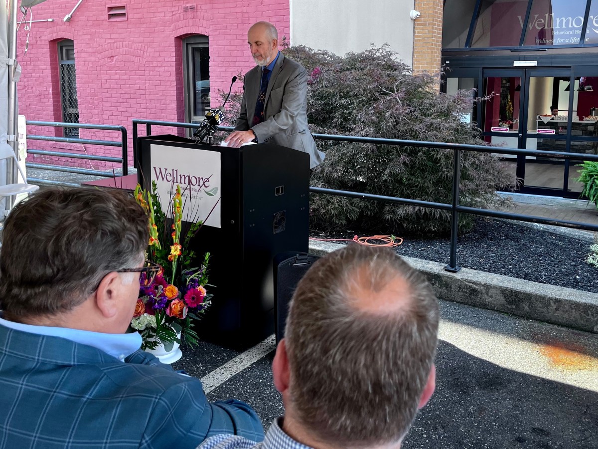 A man speaks at a lecturn in front of a building.