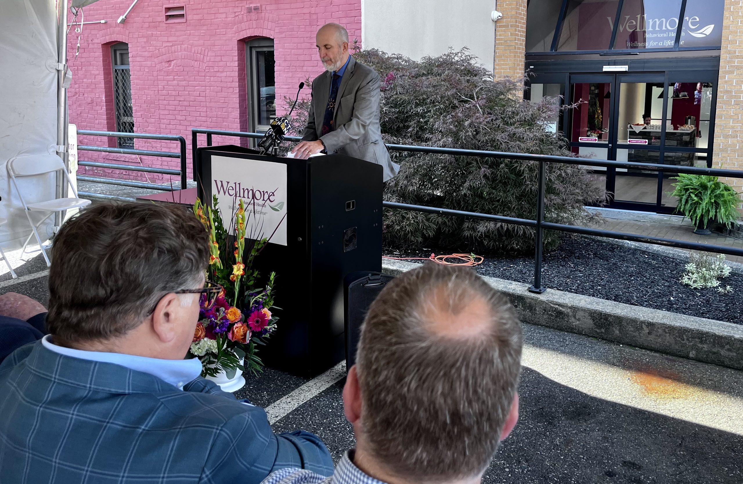 A man speaks at a lecturn in front of a building.
