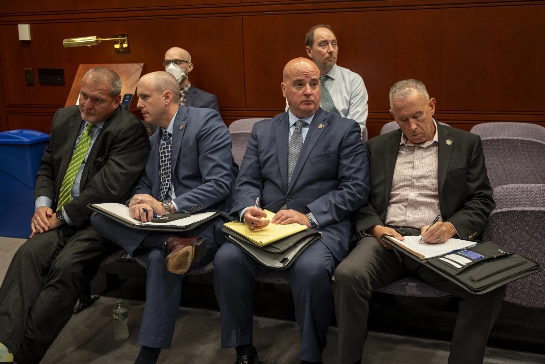 Connecticut State Police Union representative Andrew Matthews sits in a room in Hartford's Legislative Office Building. He's hold a note pad and pen. He's sitting next to other union representatives.