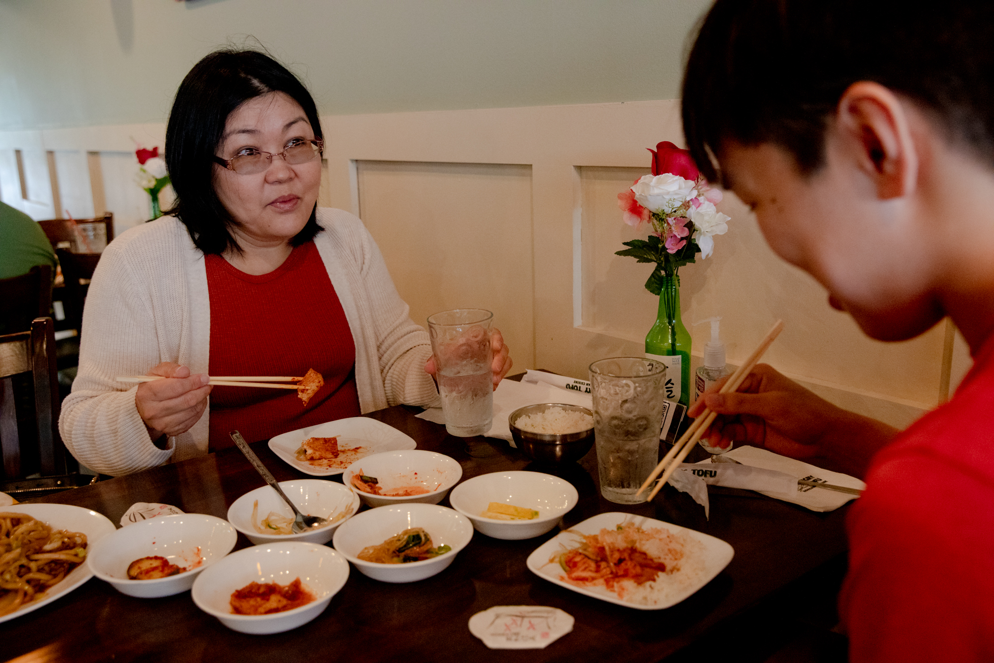 Dari Jigjidsuren sits across a table from her son, Bryson Tsogt-Erdene. They are eating with chopsticks. The table is filled with small bowls of food.