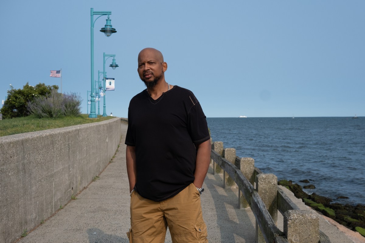 Aaron Kearney poses for a photo on a walkway near the Long Island Sound. His hands are in his pockets.