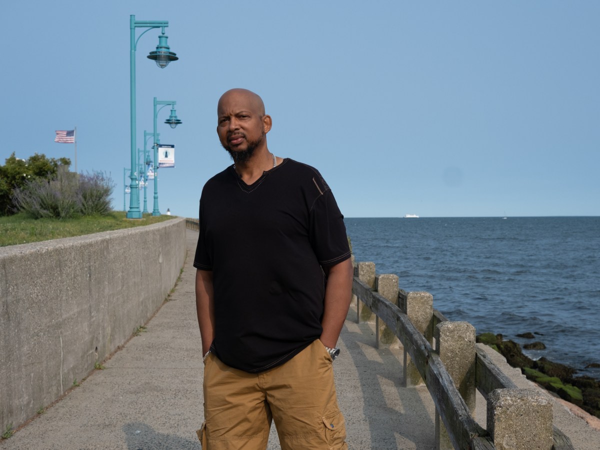 Aaron Kearney poses for a photo on a walkway near the Long Island Sound. His hands are in his pockets.
