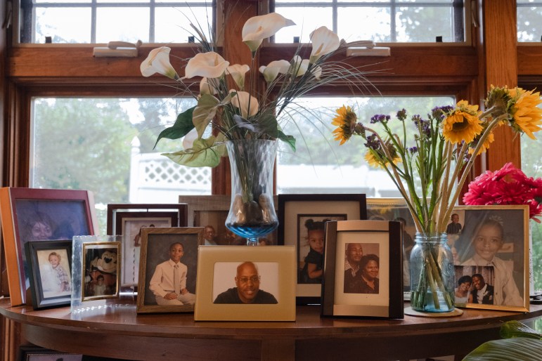 Framed family photos and a vase with flowers sit on a wooden table in Dwight Dickerson's living room.