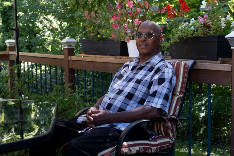 Dwight Dickerson poses for a photo while sitting in a chair. He's wearing sunglasses and his hands are folded together.