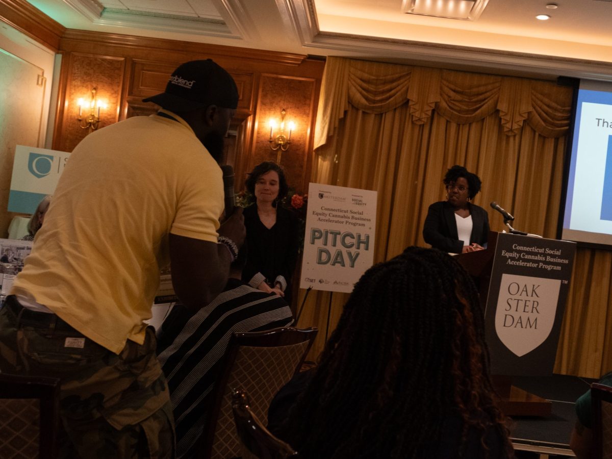 A woman at a podium answers a question from a man holding a mic in the audience.