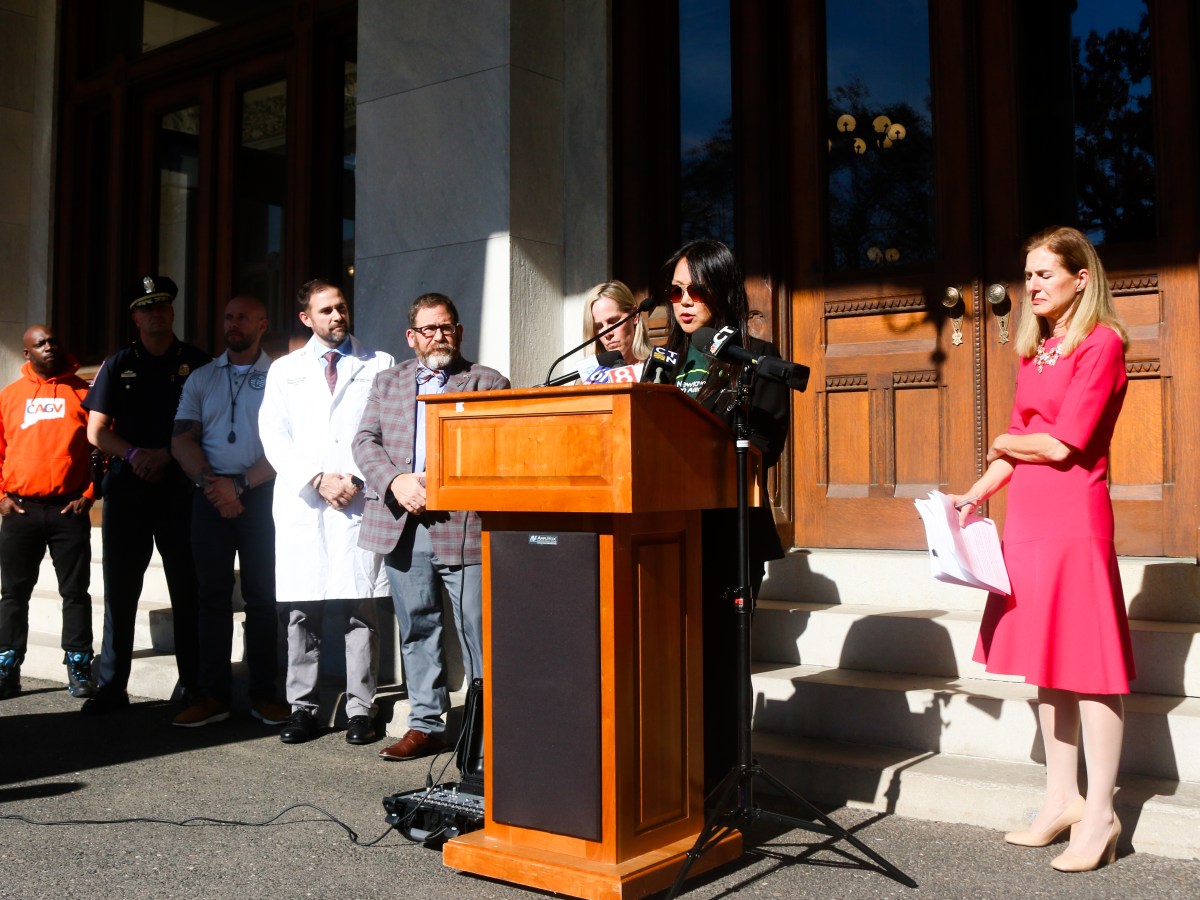 Po Murray, chair of the Newtown Action Alliance, stands behind a podium while speaking to the press. Murray is flanked by Lt. Gov. Susan Bysiewicz, health officials and law enforcement.