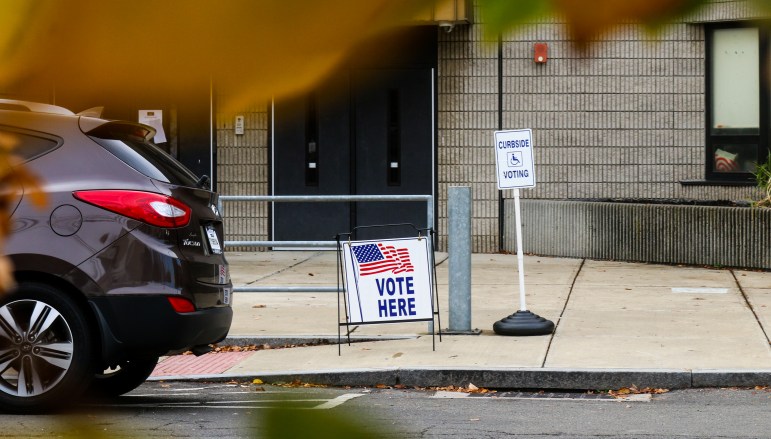 Two signs, one that says "Vote Here" and another that says "Curbside Voting," stand in front of Bridgeport's Paul Lawrence Dunbar School.