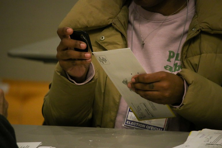 A person is stapling a white envelope while sitting at a table. The person carrying out the action is an election official.