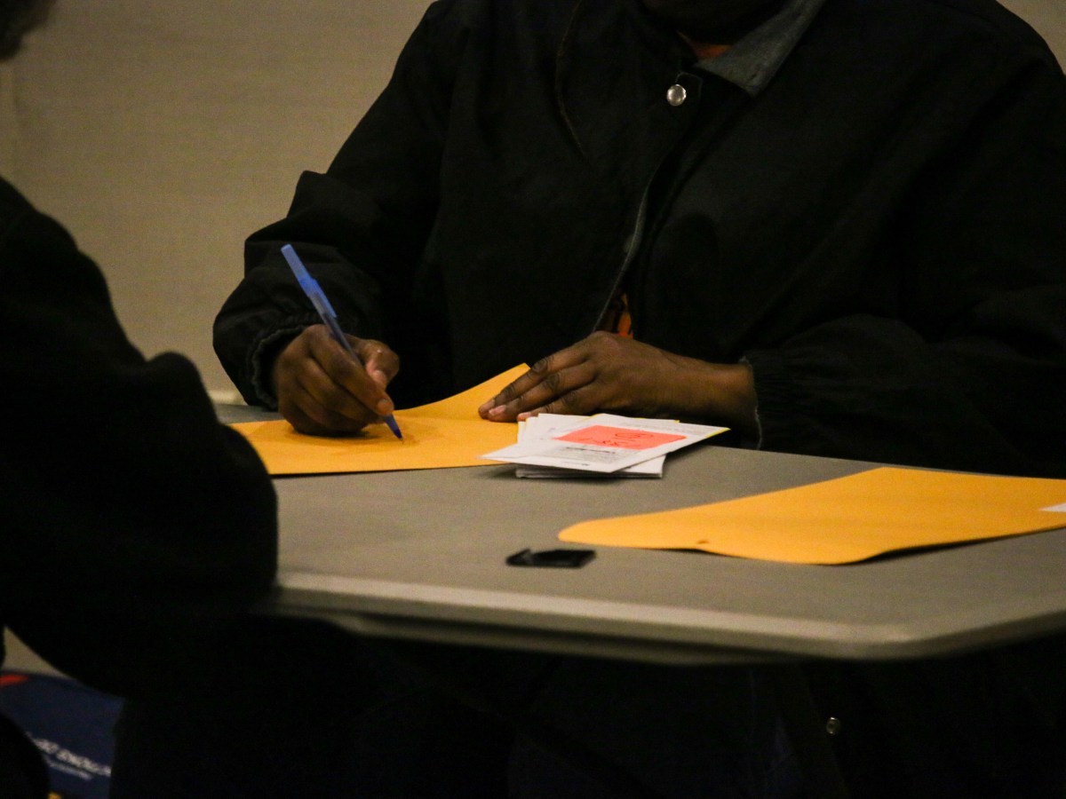 An election worker sits at a table and writes on a gummed envelope with a blue pen.