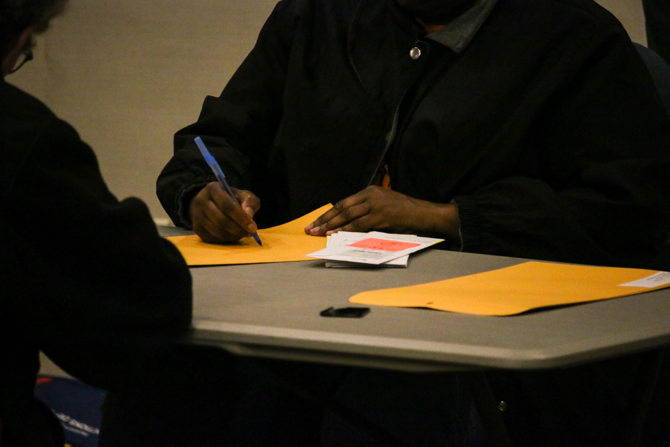 An election worker sits at a table and writes on a gummed envelope with a blue pen.