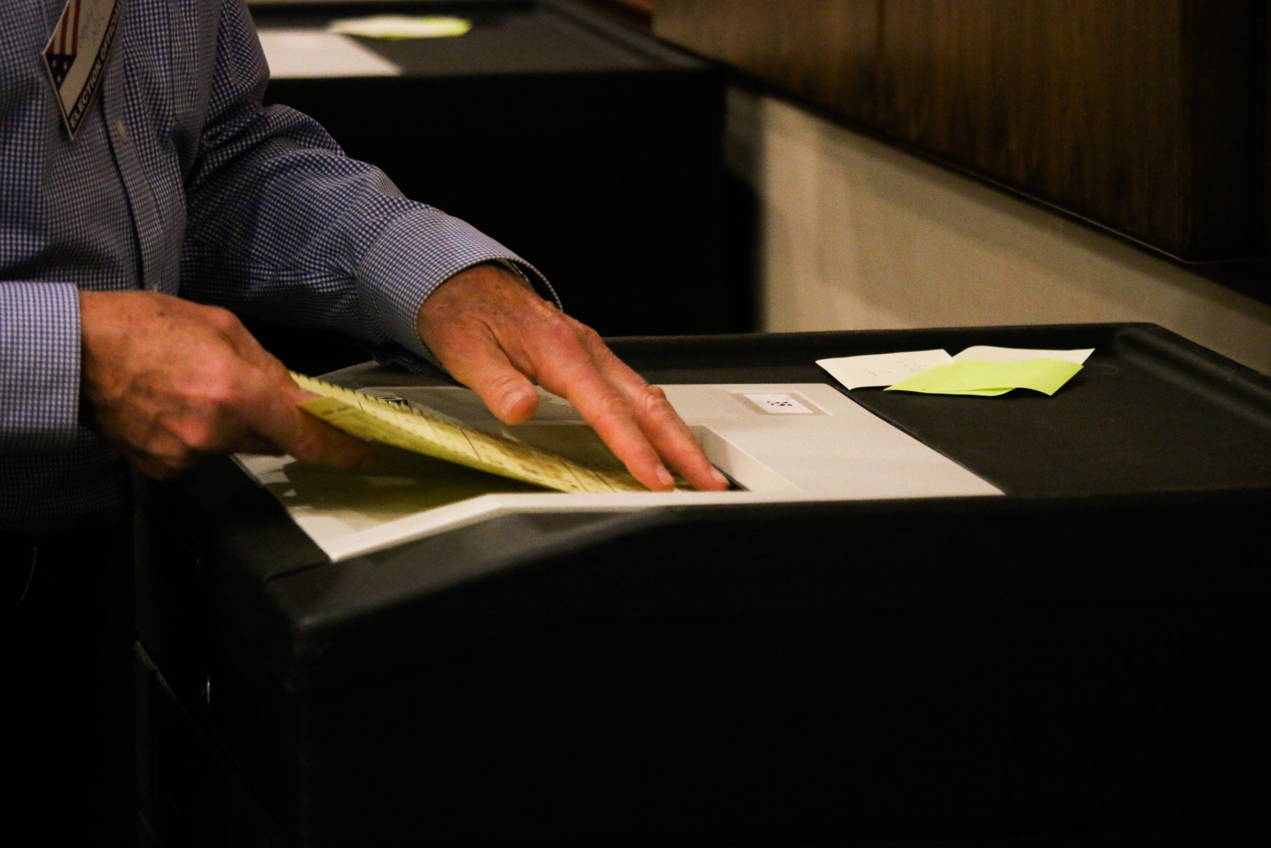 Hands are seen inserting an election ballot — a piece of yellow paper — into a machine that calculates vote totals.