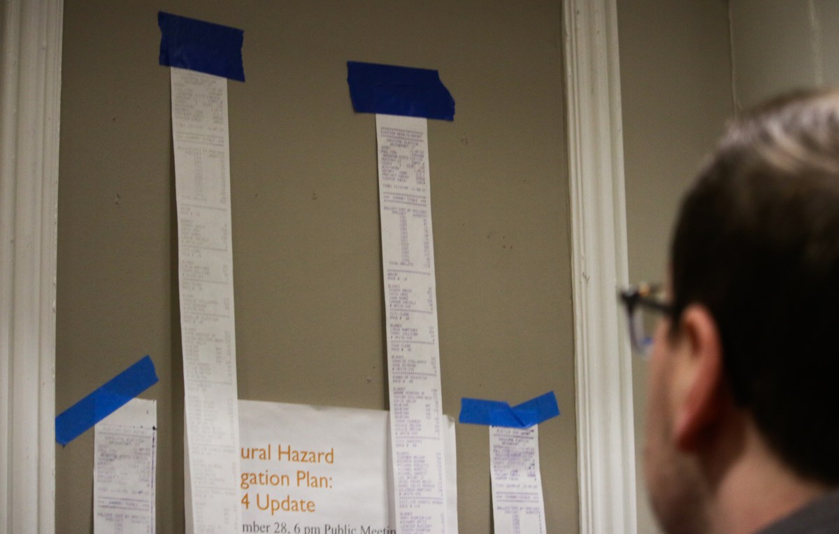 Receipt-like paper sits taped to a wall, showing absentee ballot results in Bridgeport's mayoral election. A person can be seen looking at totals.