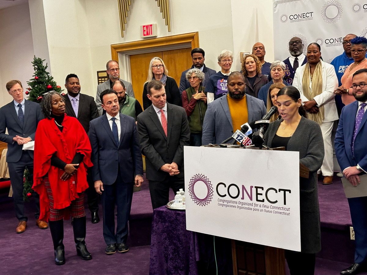 A group of Connecticut residents, lawmakers and advocates stand behind and on the side a person speaking at podium inside of a New Haven church. All of the people are at a gathering to announce the full rollout of Connecticut's "clean slate" law, which automatically erases misdemeanors and low-level felonies from the criminal records of some people.