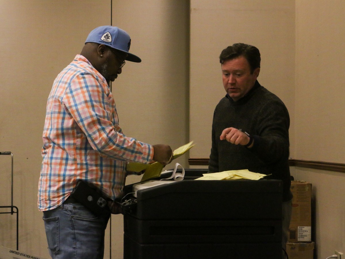 Tim DeCarlo, one of two Bridgeport election monitors, is talking and working with an election worker during the process of placing absentee ballots inside of a machine.