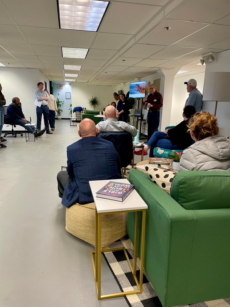 Seated people watch a man make a presentation.