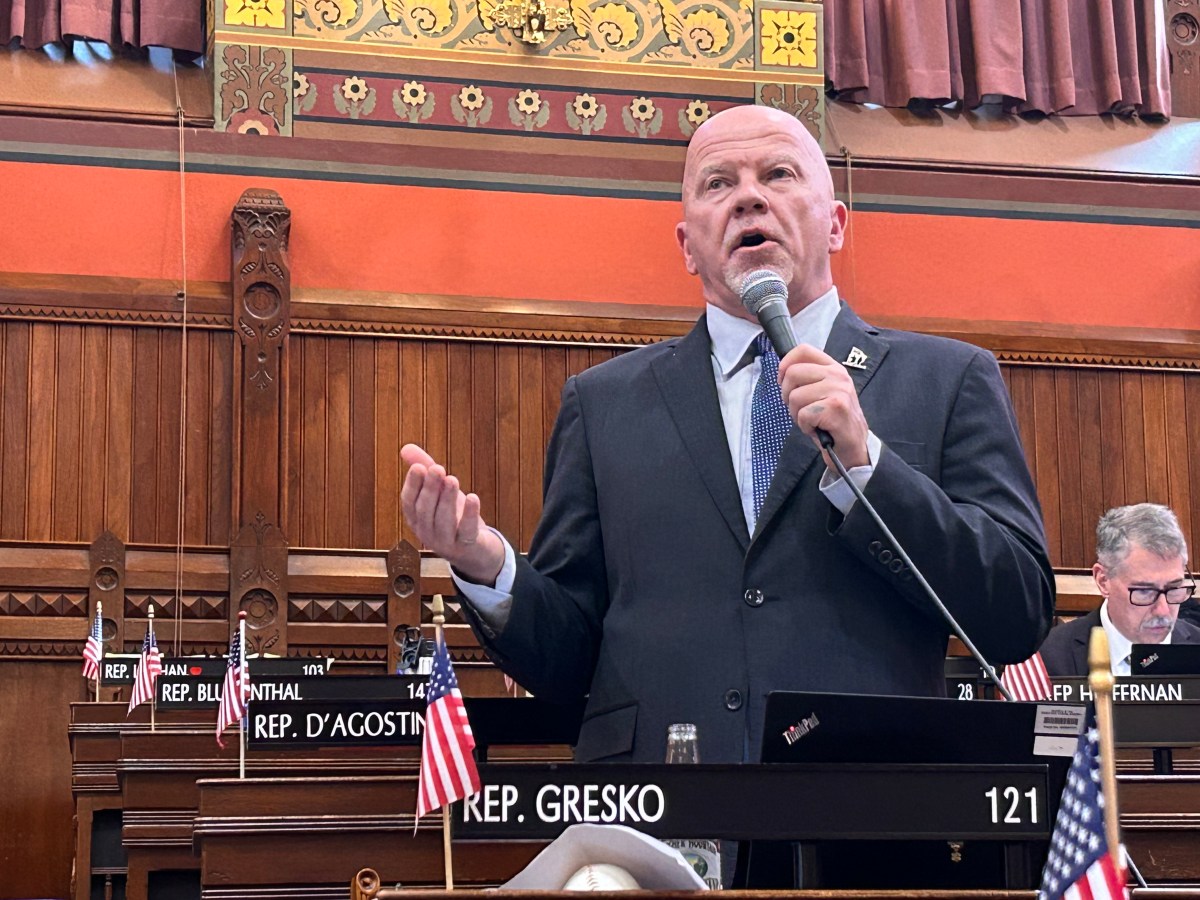 A man in a suit stands with a microphone on the House floor.