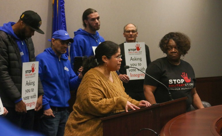 Marisol Garcia is speaking into a microphone at a podium while five people are standing near her and listening.