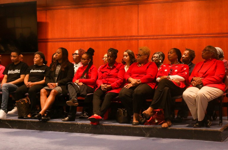 A group of people are seen sitting next to each other and looking off at someone who's speaking.