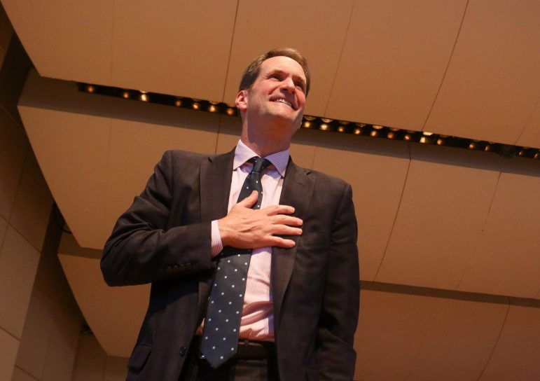 Jim Himes is standing and looking off into a crowd, with his hand resting slightly below his chest as a sign of gratitude for the applause.