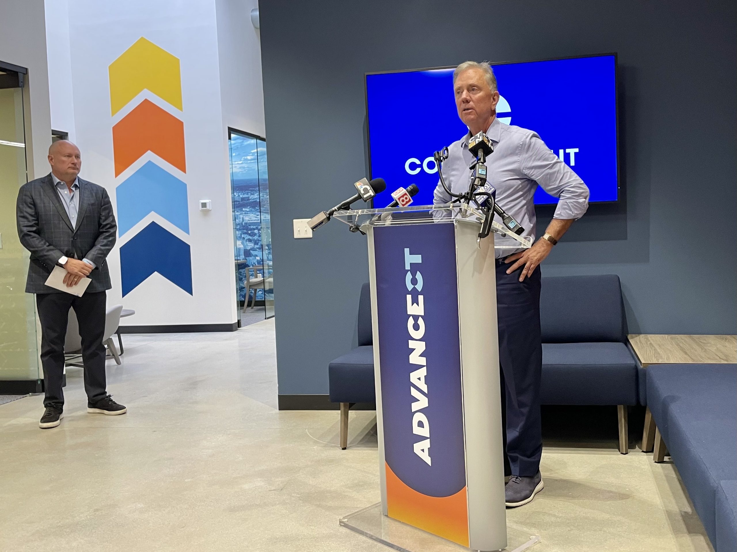 The governor stands at a podium emblazoned with the logo for AdvanceCT.