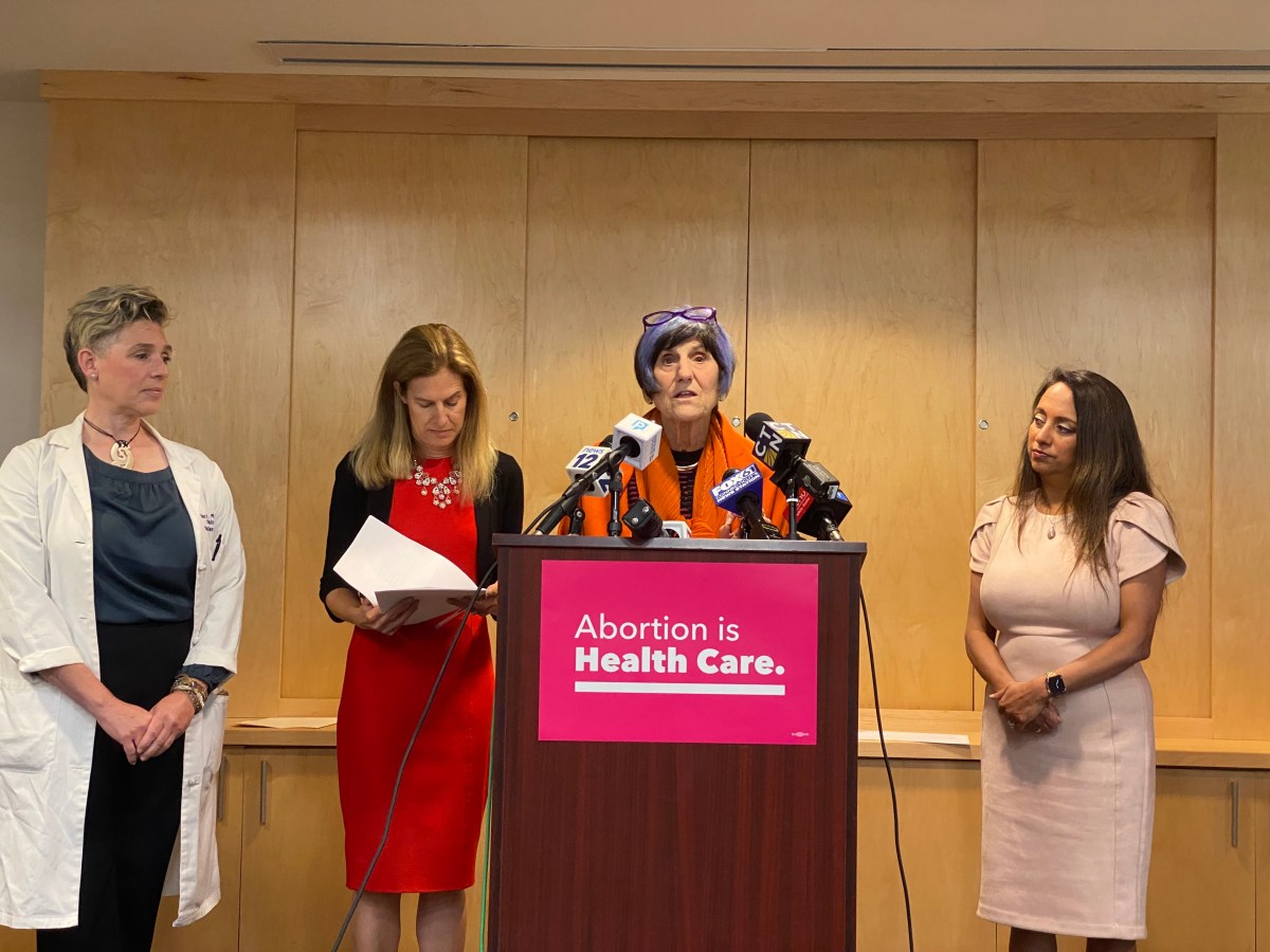 A woman stands at a podium, which has a sign on it that reads "Abortion is Health Care."