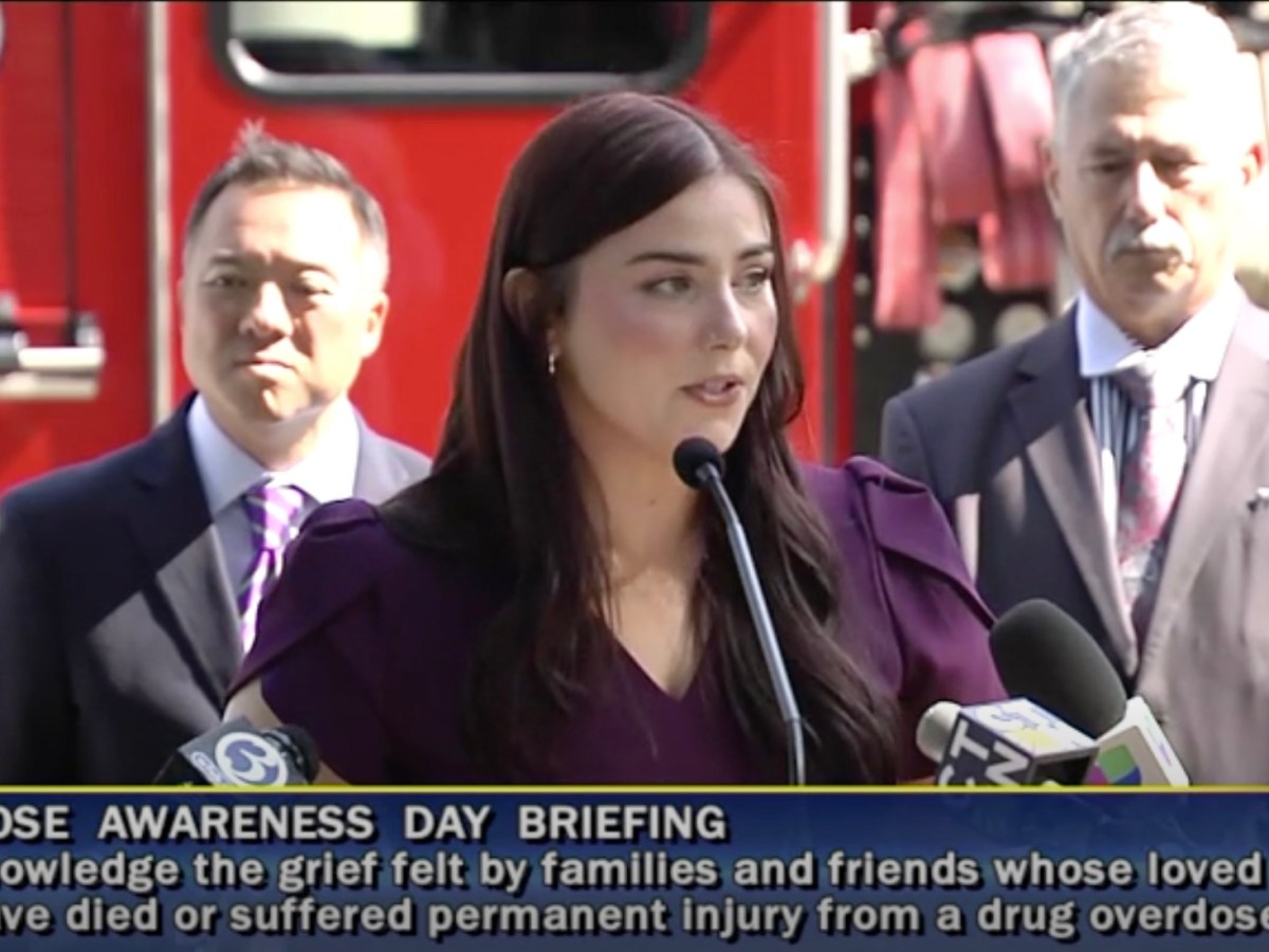A woman stands in front of a firetruck and speaks into a microphone at a podium.