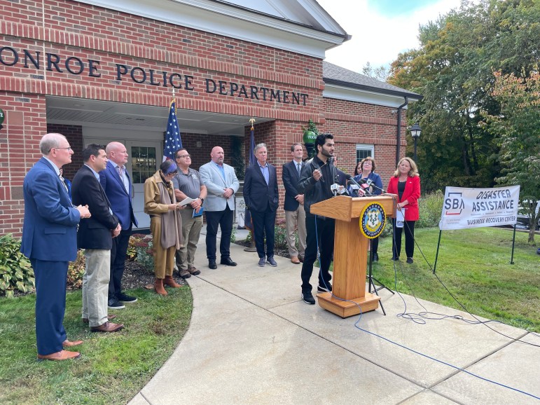 Local, state and federal leaders stand outside the Monroe Police Department as a business owner speaks at a podium.