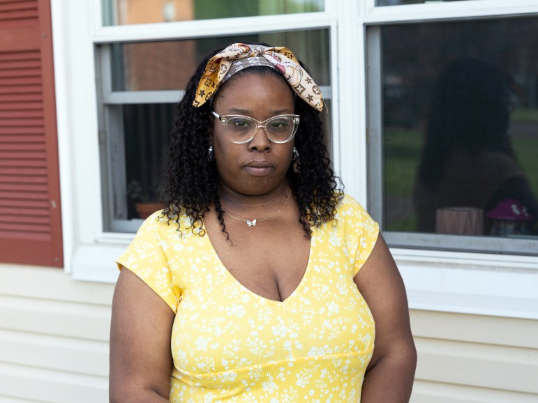 Carr, a woman wearing glasses and a bandana, stands outside of a house.